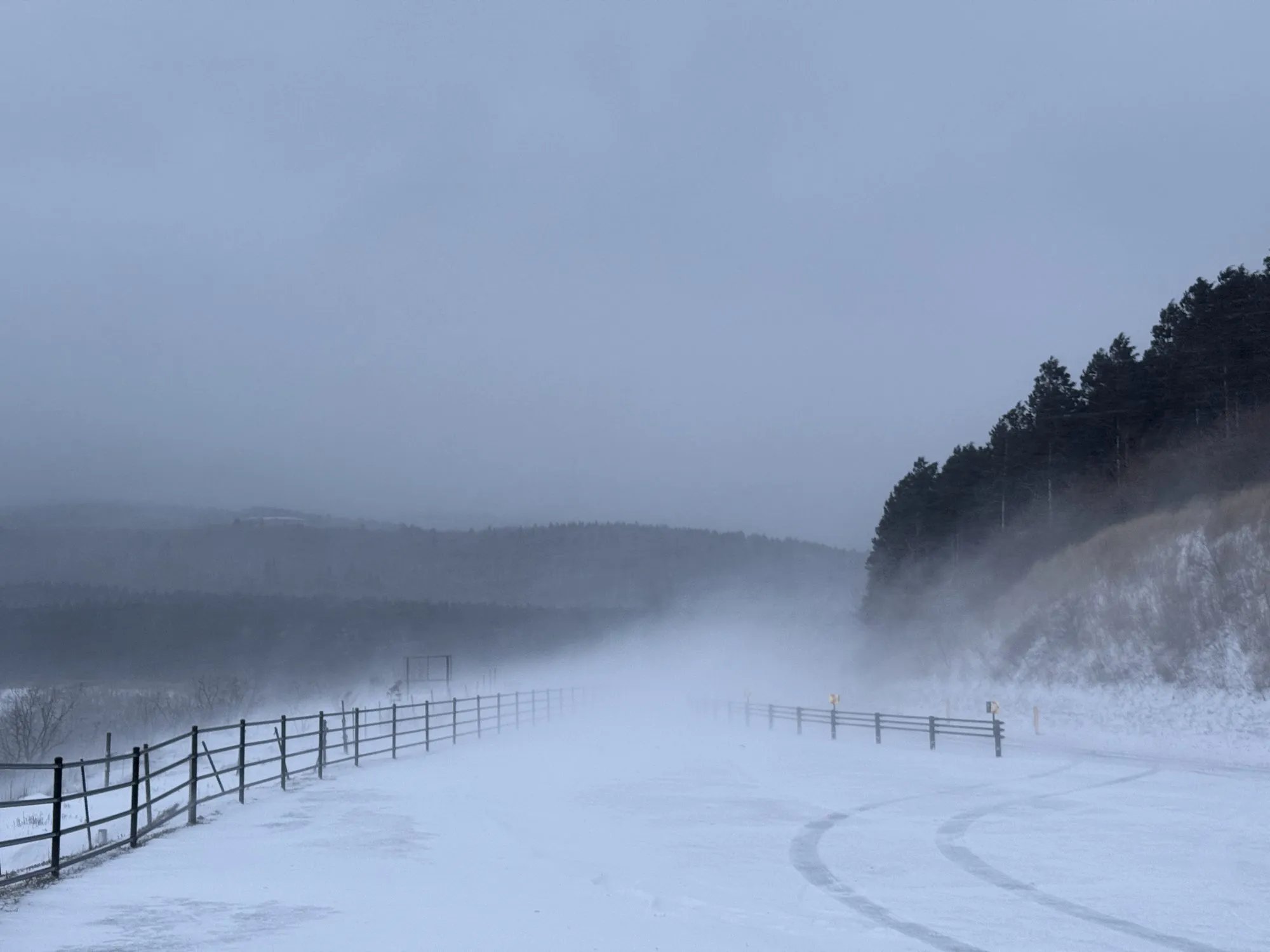 Blowing snow reducing visibility to almost nothing across an open road near Aso, fence posts disappearing into white