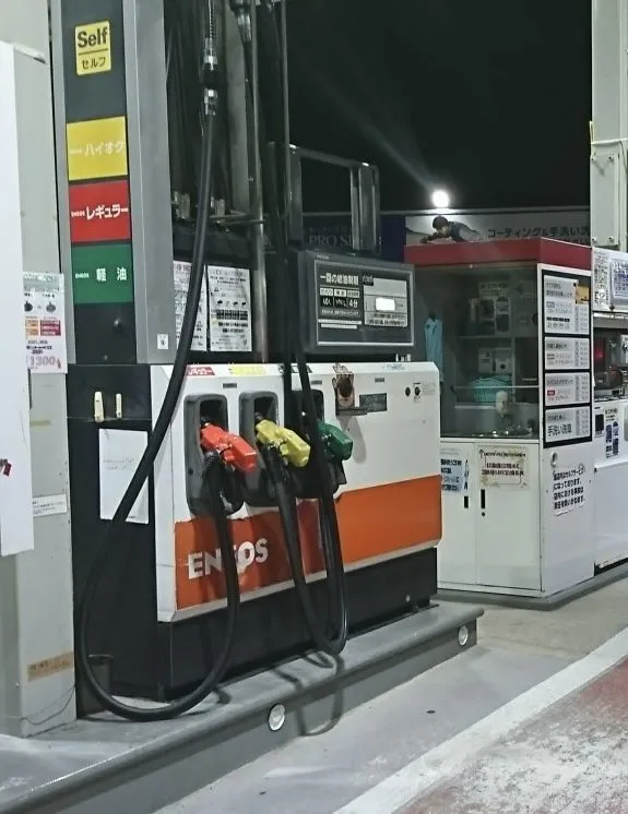 A self-service petrol pump in Japan with three nozzles side by side — red, yellow and green — beside a column labelled ハイオク, レギュラー and 軽油