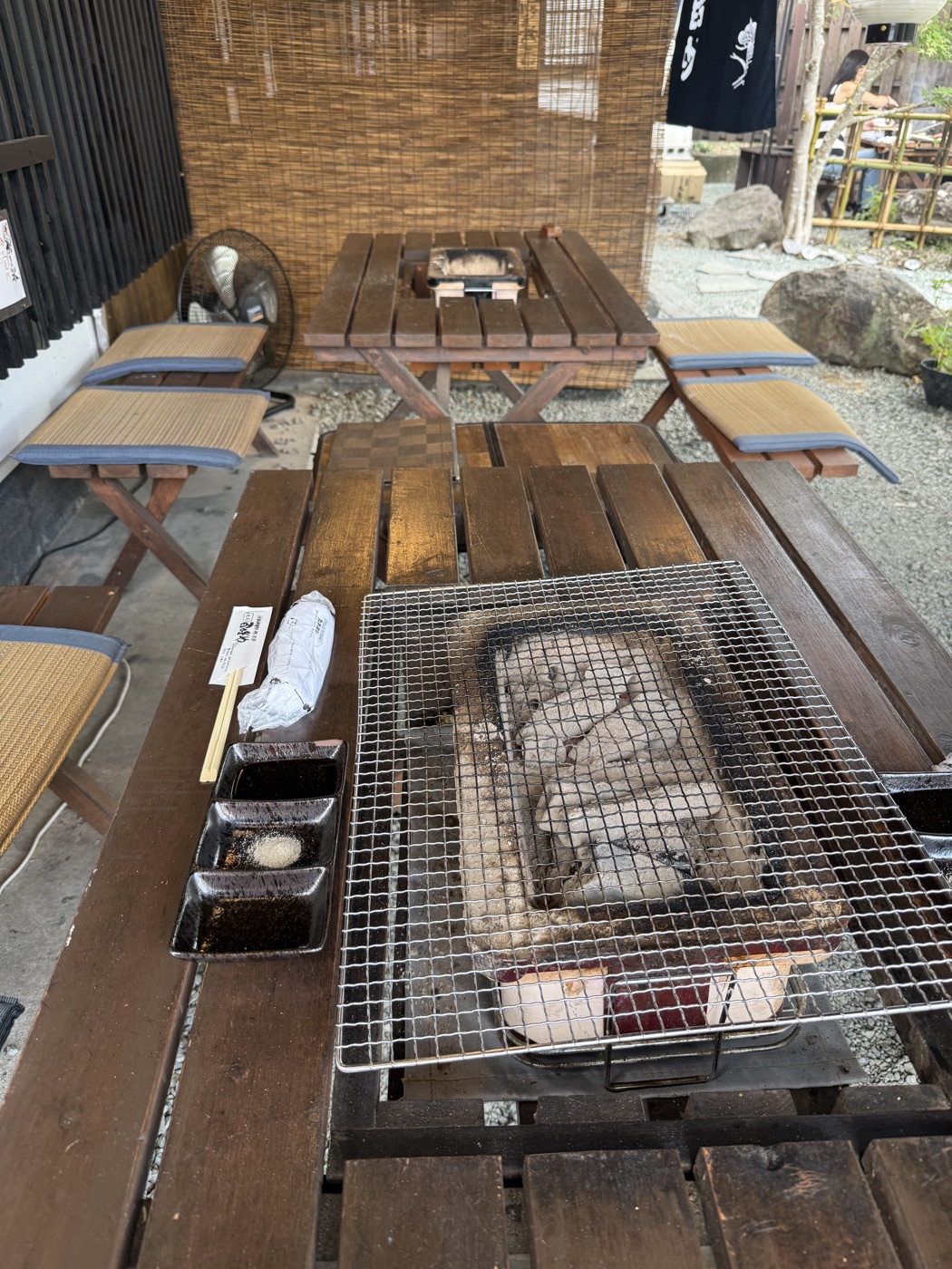 木のテーブルの中央に炭火と焼き網。手前にタレ皿が並ぶ